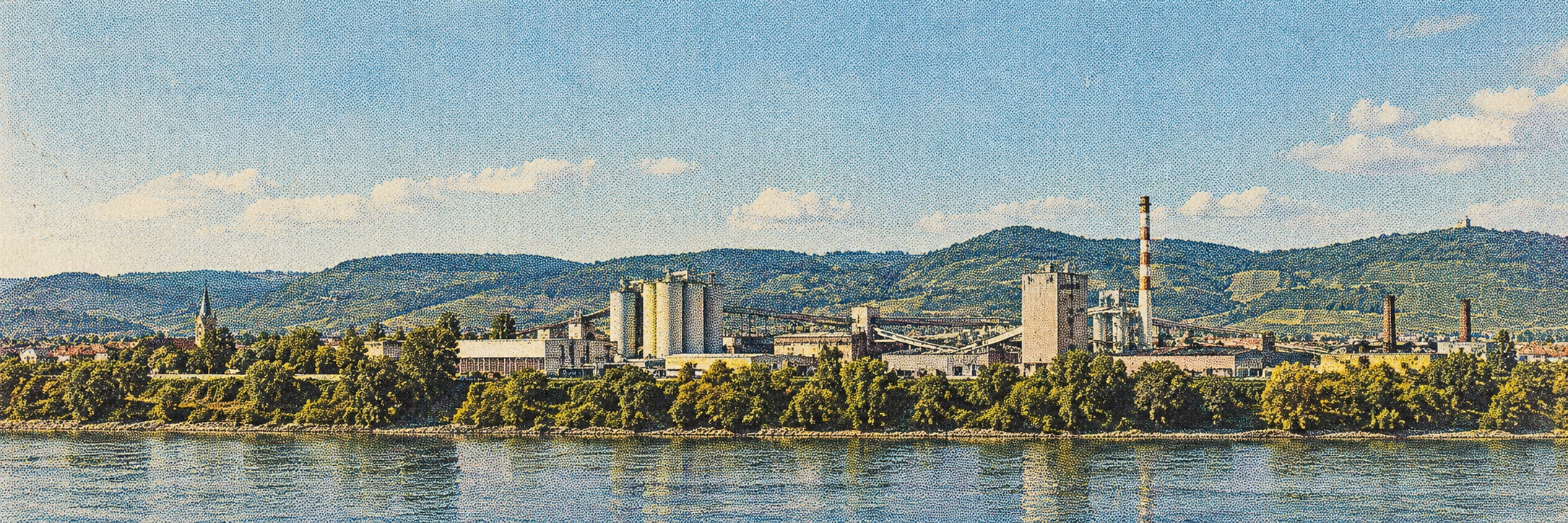 Illustrative industrial site beside a river with green hills.
